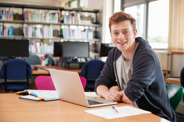 Portrait Of Male Student Working At Laptop In College Library